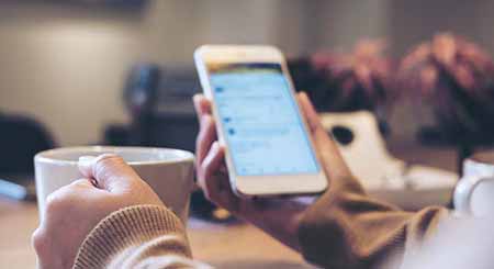 Woman checking social media on phone while drinking coffee.