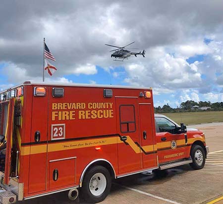 EMS and HFF Brevard County Fire Rescue Paramedic Unit truck in foreground with helicopter flying overhead.