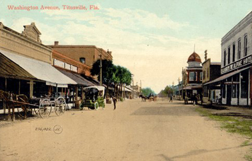 Washington Aveue in Titusville, Florida from late 1800's. A couple horsedrawn carriages and an automobile appear on an empty dirt road.