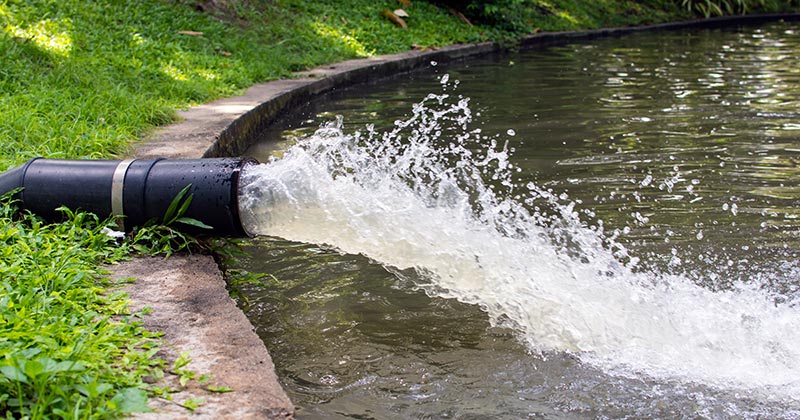 A pipe with water being dumped into a retention pond.