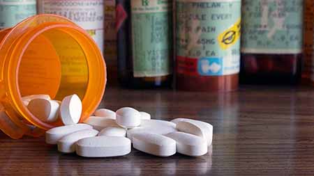 Multiple prescription bottles, one is tipped over with pills spilled onto table.