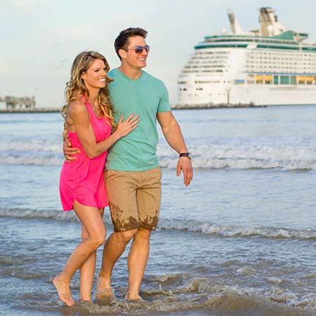 Young couple walking on the beach with a cruise ship in the background.